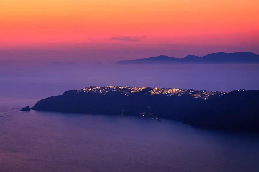 A stunning sunset photo from Santorini. Taken from the cliffs of Imerovigli looking towards the town of Oia. A gorgeous glowing sunset and lights of the town all add to this stunning scene. Santorini, Greece. 