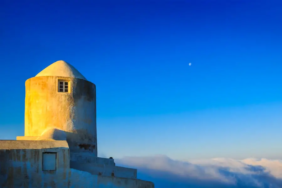 Windmill building overlooking low clouds at sunrise on Santorini